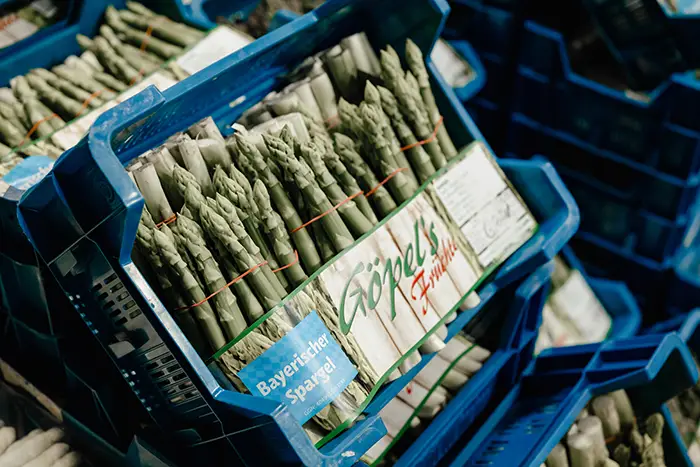 grüner Spargel mit einer Göpels-Banderole in blauen Plastik-Steigen